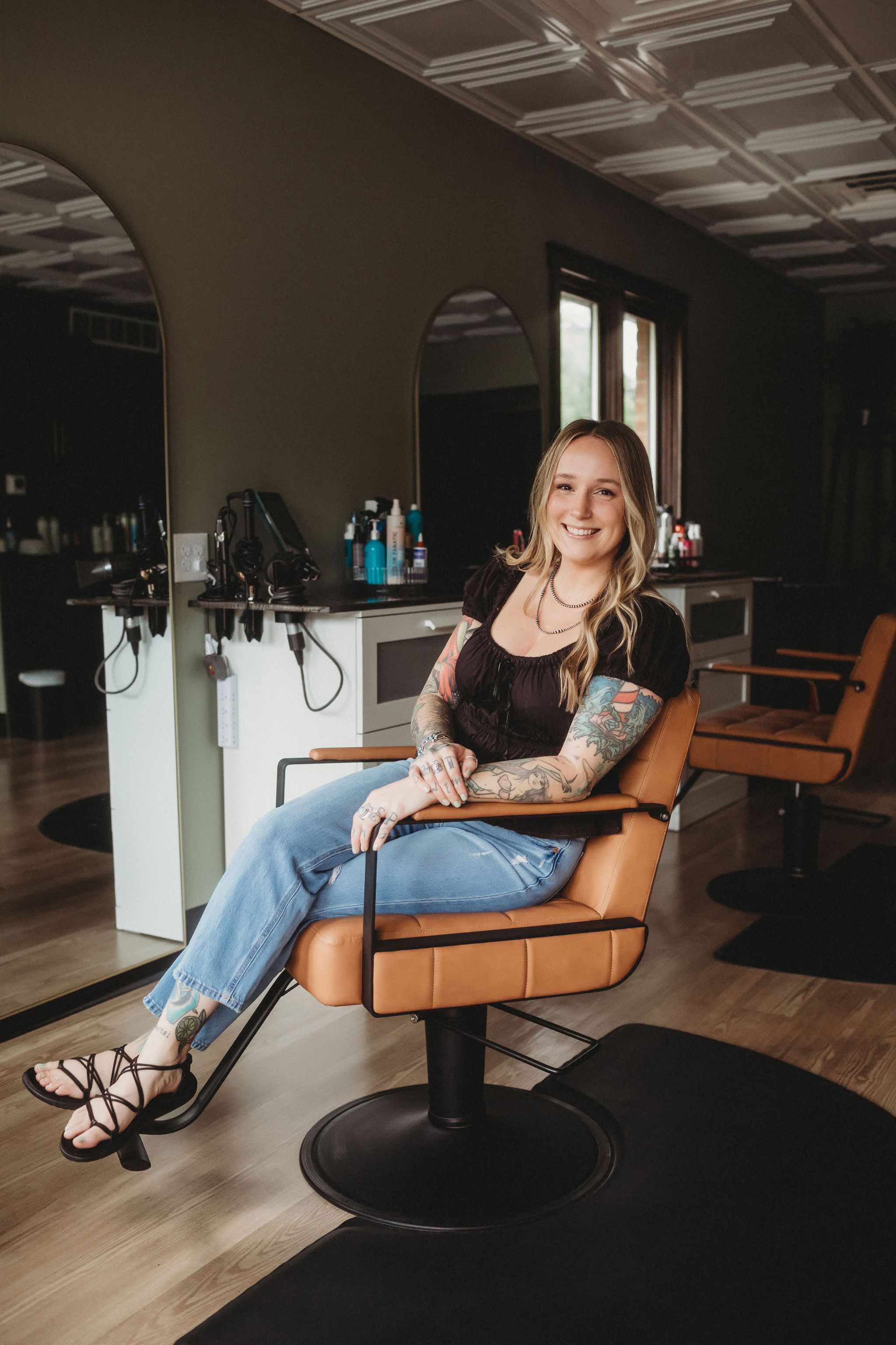 Olivia, owner of Everfern Hair Collective, seated in a tan styling chair